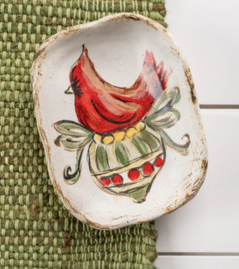 A ceramic ornament featuring a hand-painted red cardinal design on a white and green background, placed on a woven mat.