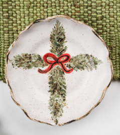A ceramic holiday decoration featuring a Christian cross with evergreen branches and a red bow on a white background.