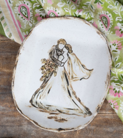 A hand-painted ceramic plate featuring a couple making a heartfelt wedding vow, with a bouquet of flowers in their hands. The plate has a rustic finish and floral pattern in the background.